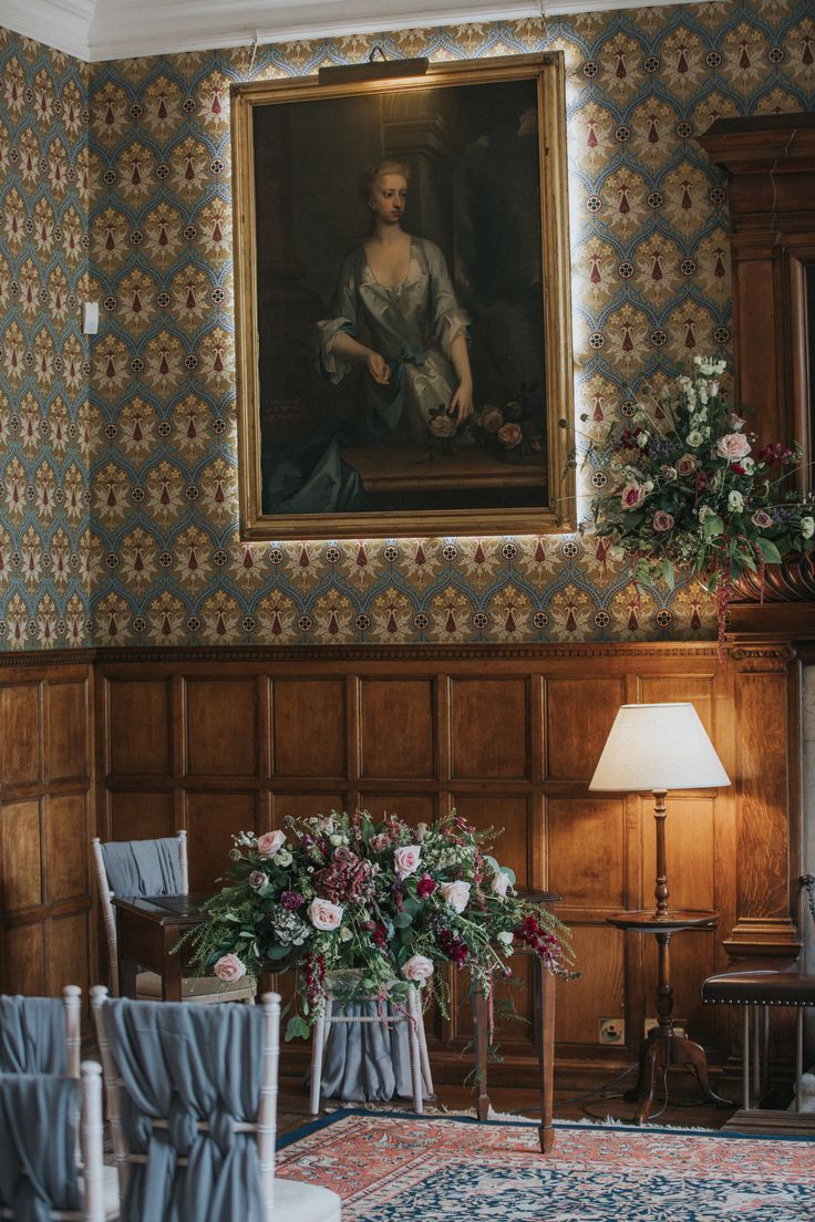 a painting hanging on the wall in a living room with chairs and vases filled with flowers