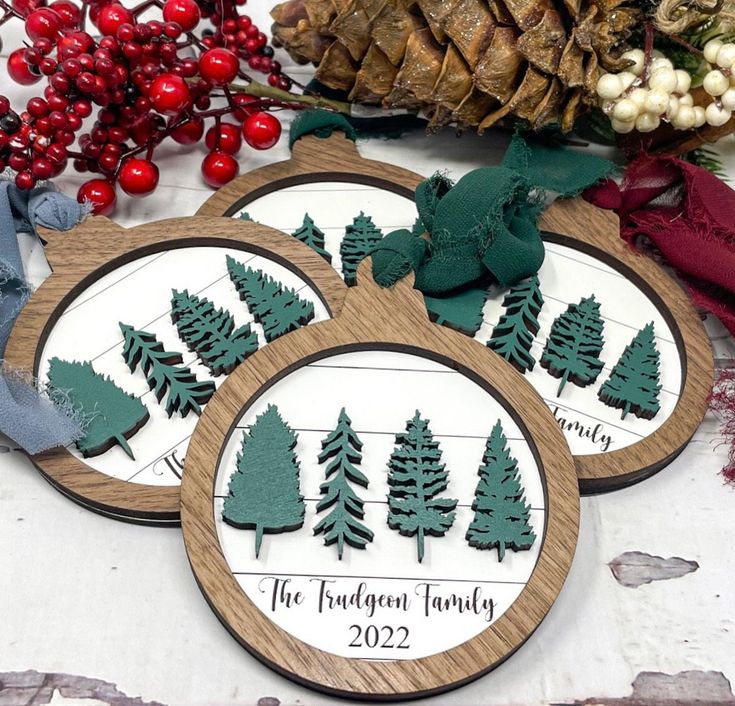 three wooden coasters with trees on them next to pine cones and other holiday decorations