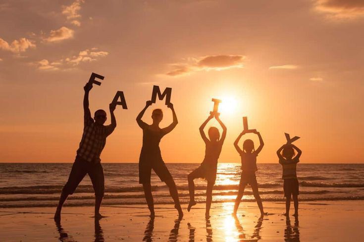 four people standing on the beach with their arms in the air holding up letters that read fam