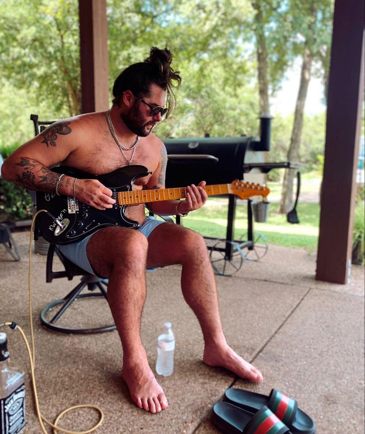 a man sitting in a chair playing an electric guitar on the porch with his feet propped up