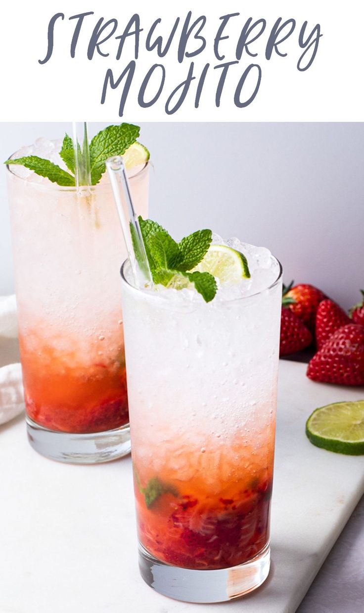 two glasses filled with ice and strawberries next to limes on a cutting board