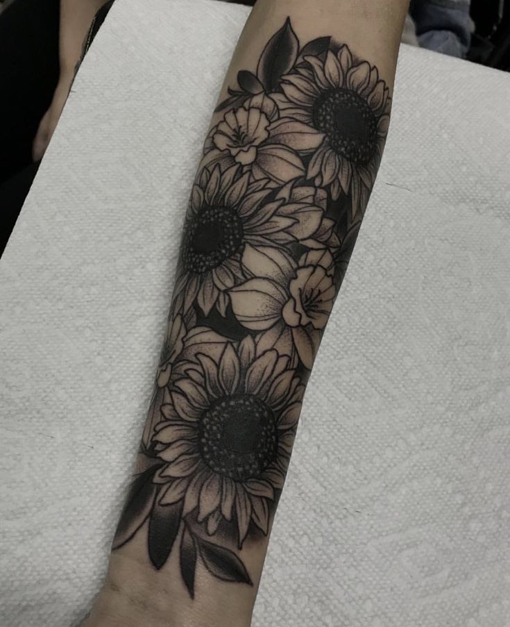 black and white sunflowers tattoo on the left arm, with dark petals around them