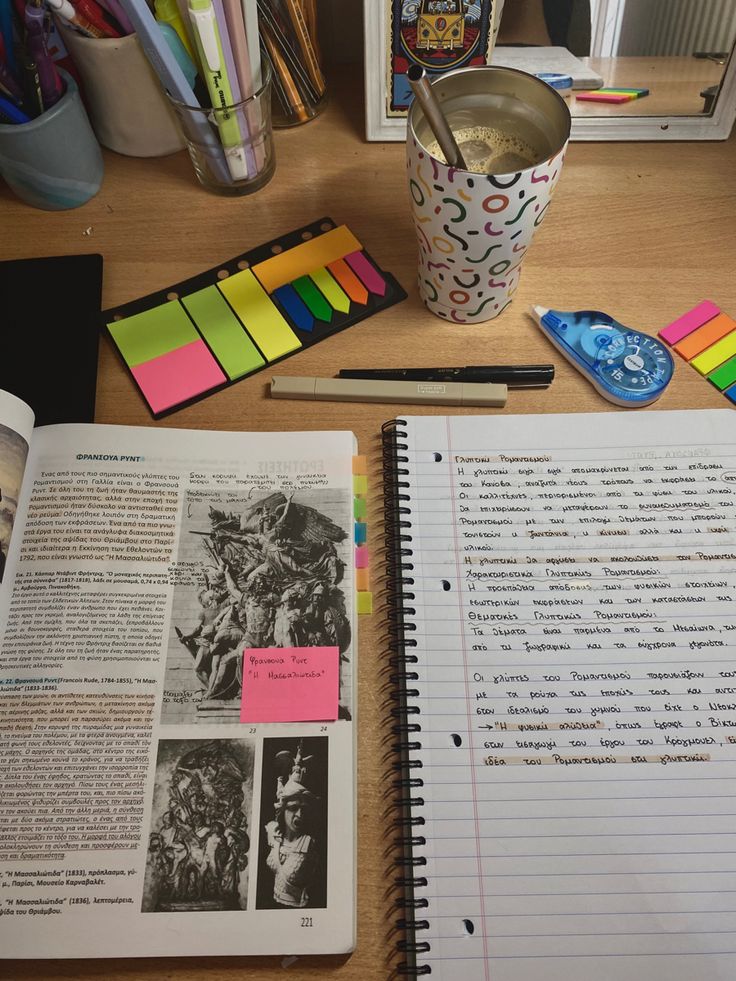 an open book on a desk next to a cup and some other office supplies with sticky notes