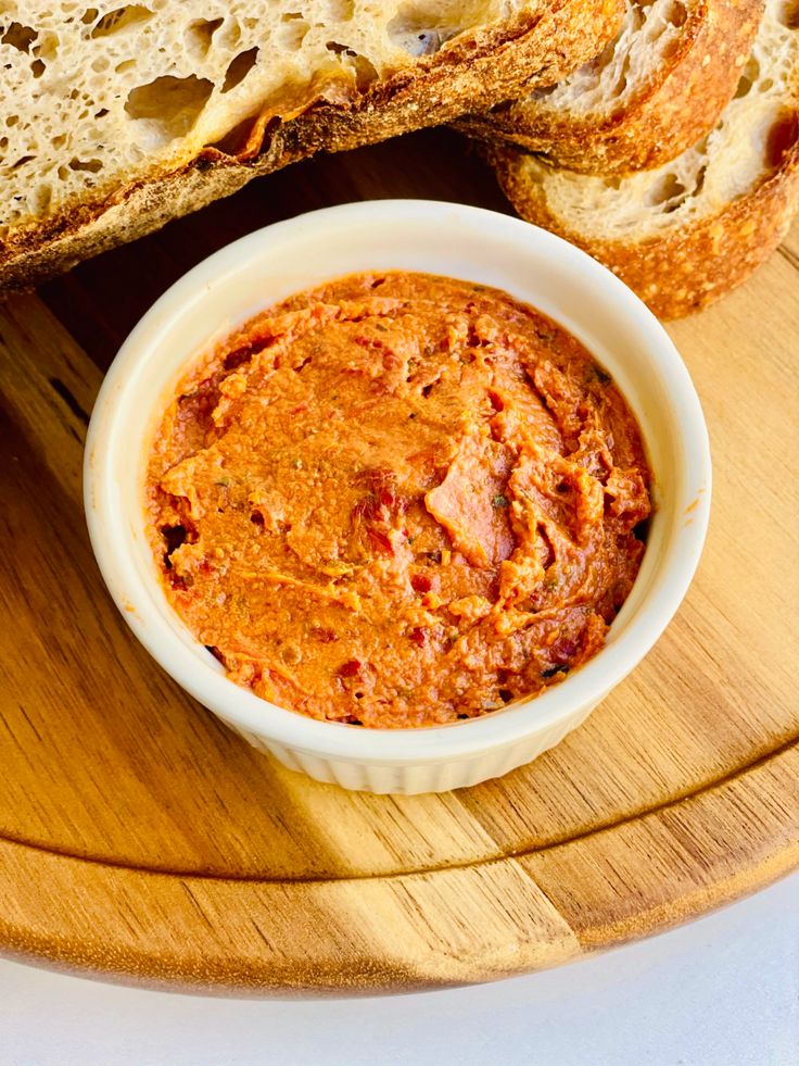 a bowl of hummus next to some bread on a cutting board