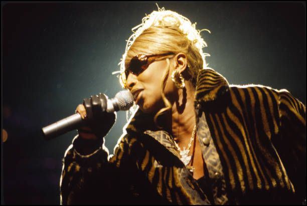 a woman holding a microphone in her right hand and wearing sunglasses on top of her head