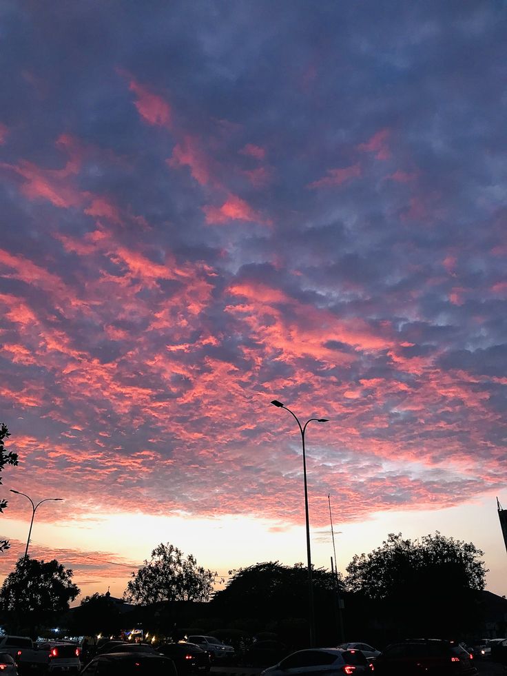 the sky is pink and purple as cars are parked on the side of the road