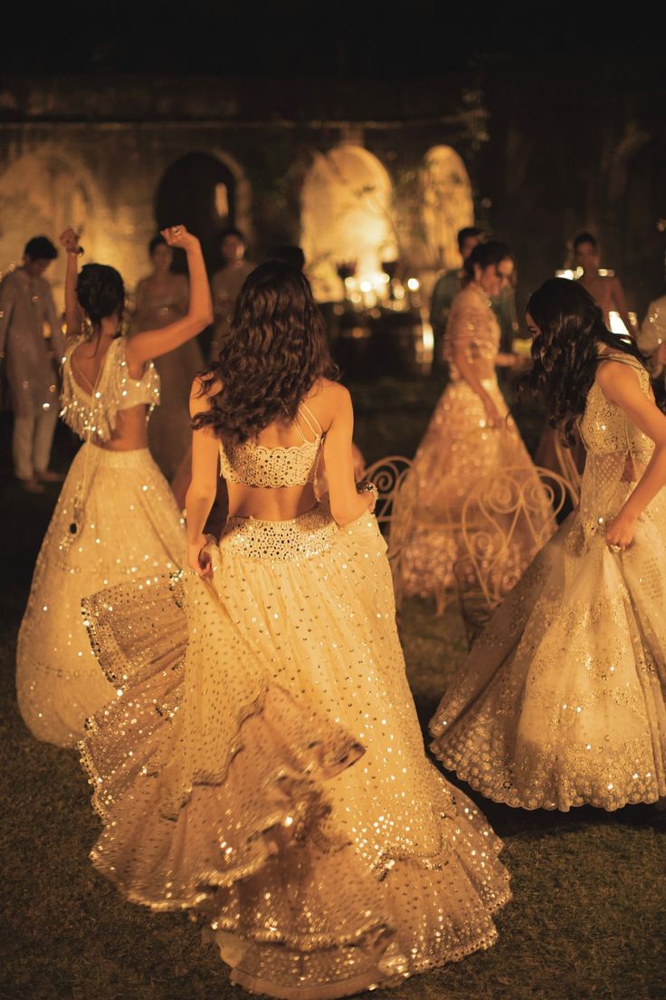 several women dressed in gowns are dancing on the grass at an outdoor event with candles lit behind them