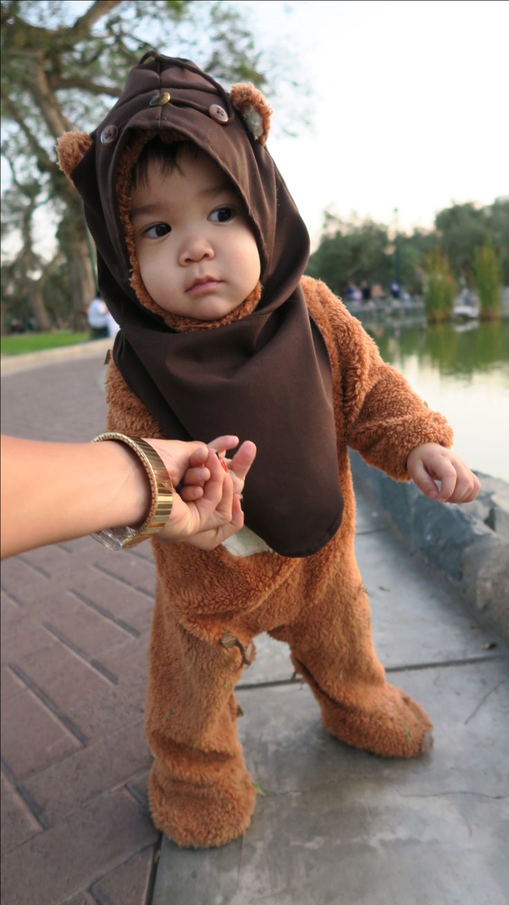 a baby dressed in a bear costume is being held by someone's hand while standing on the sidewalk