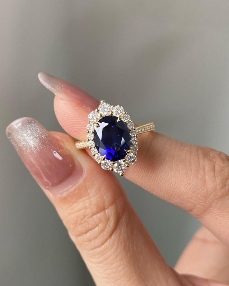 a woman's hand holding an engagement ring with a blue sapphire and diamond halo