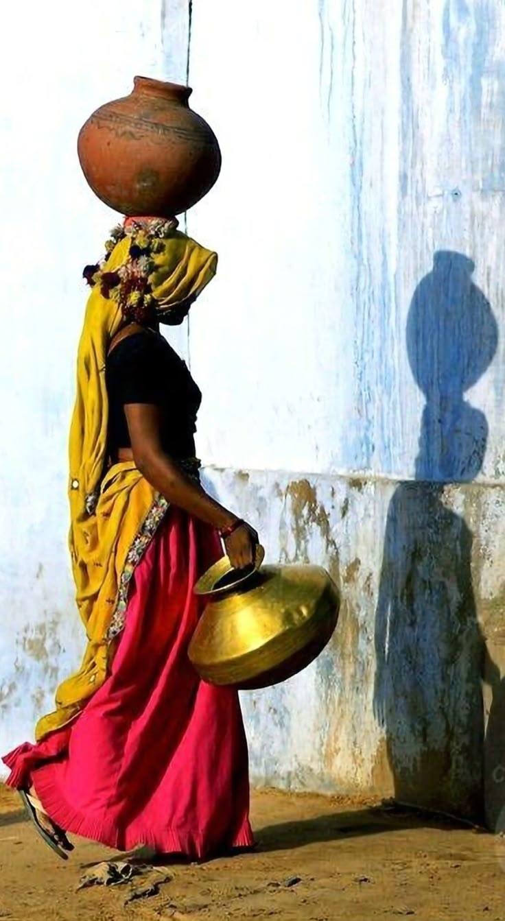 a woman walking down the street carrying a pot on her head