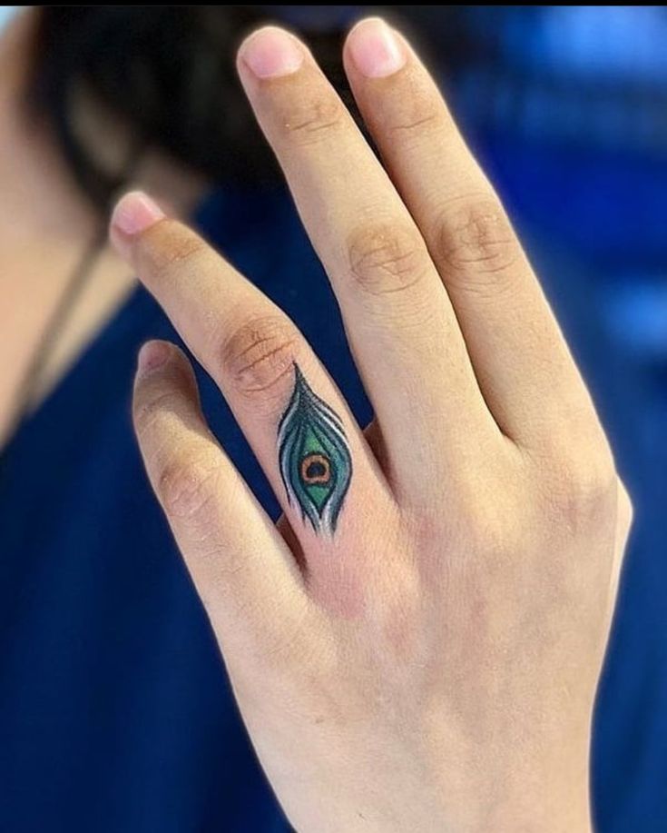 a woman's hand with a peacock feather tattoo on the middle finger and ring