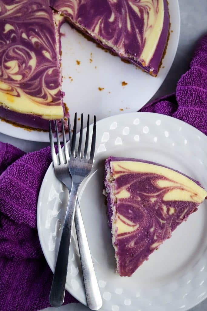 a piece of cheesecake on a white plate with a fork and purple napkin next to it