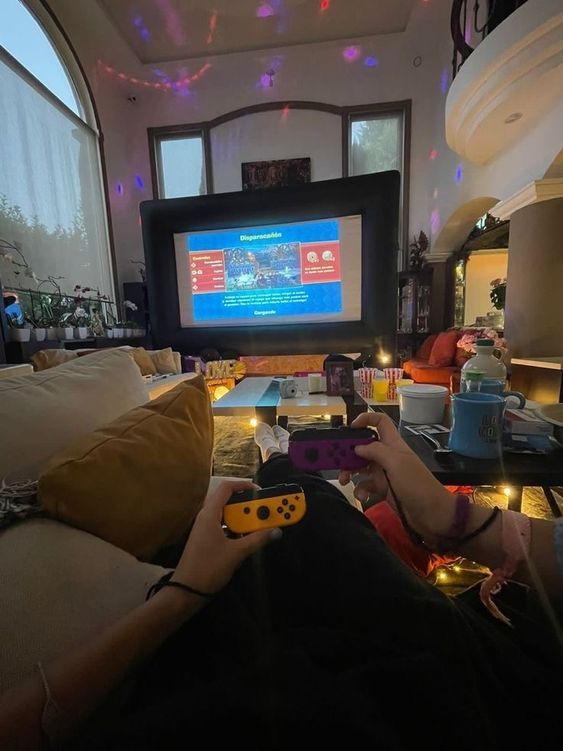 a person sitting on a couch holding a nintendo wii game controller in front of a tv