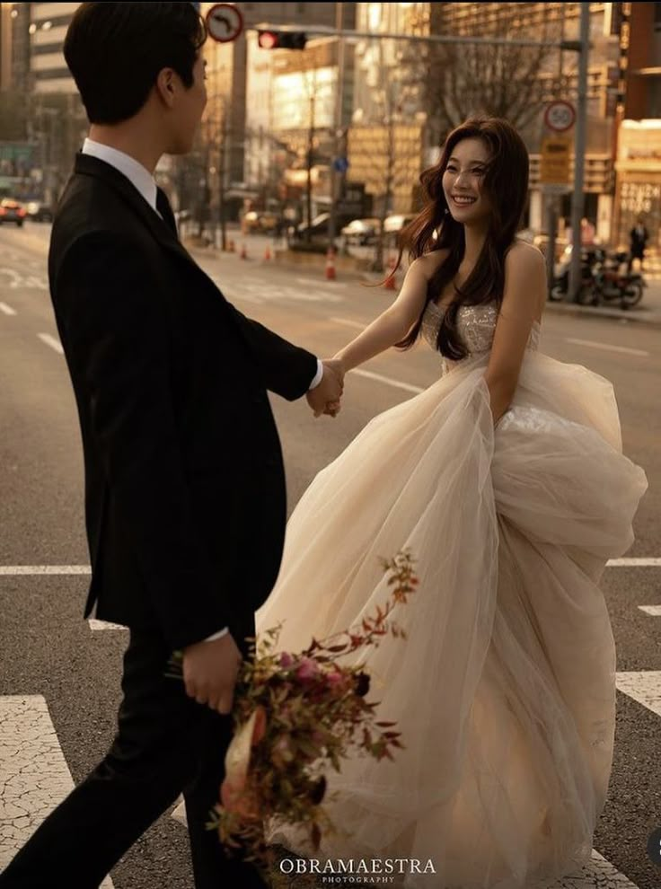 a man and woman are walking across the street holding hands while dressed in formal wear