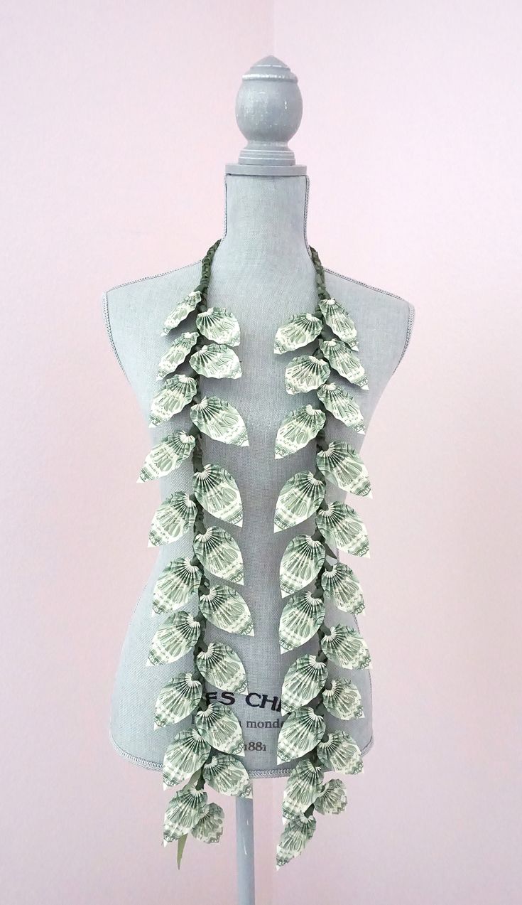 a white mannequin with green leaves on it's neck and two necklaces hanging from the back