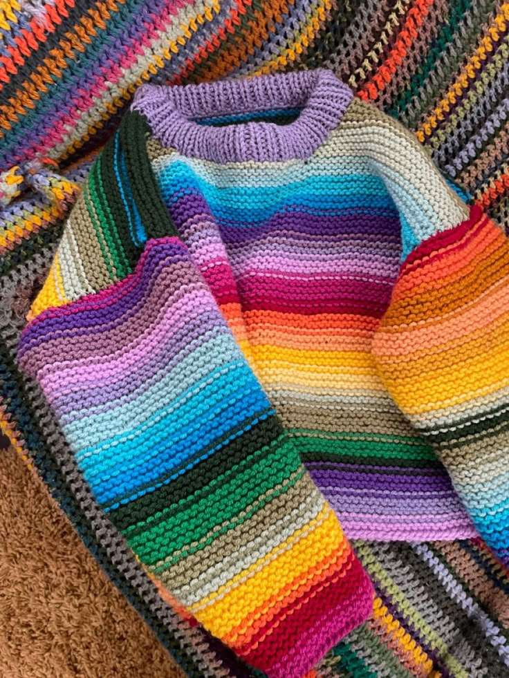 a multicolored crocheted sweater laying on top of a brown carpet next to a pair of scissors