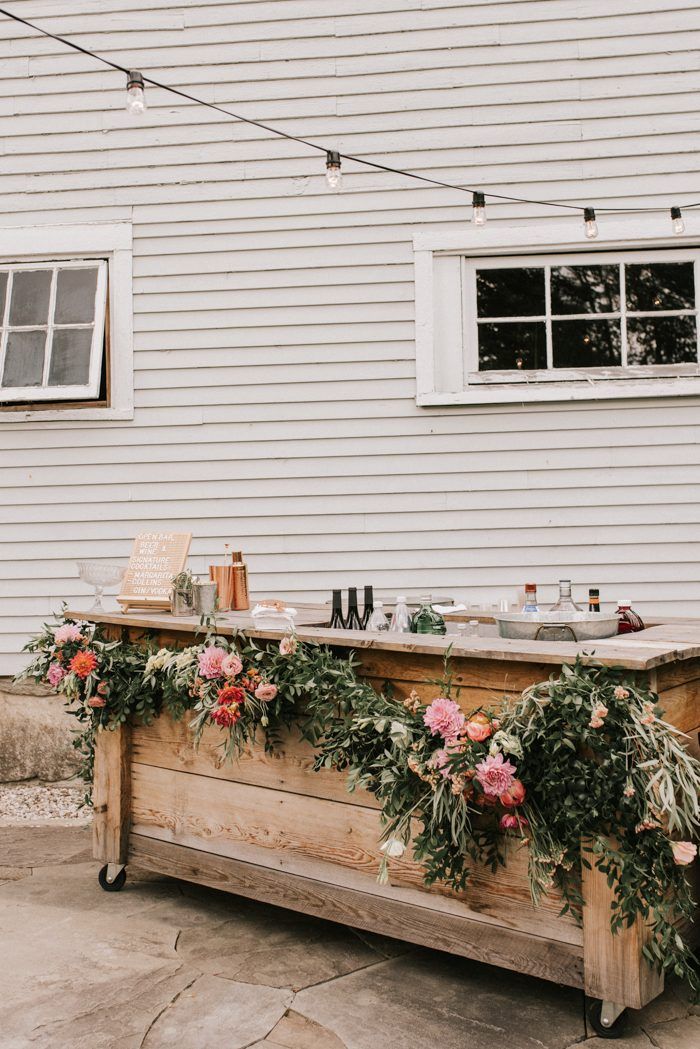 an outdoor bar is decorated with flowers and greenery for a wedding reception at the barn