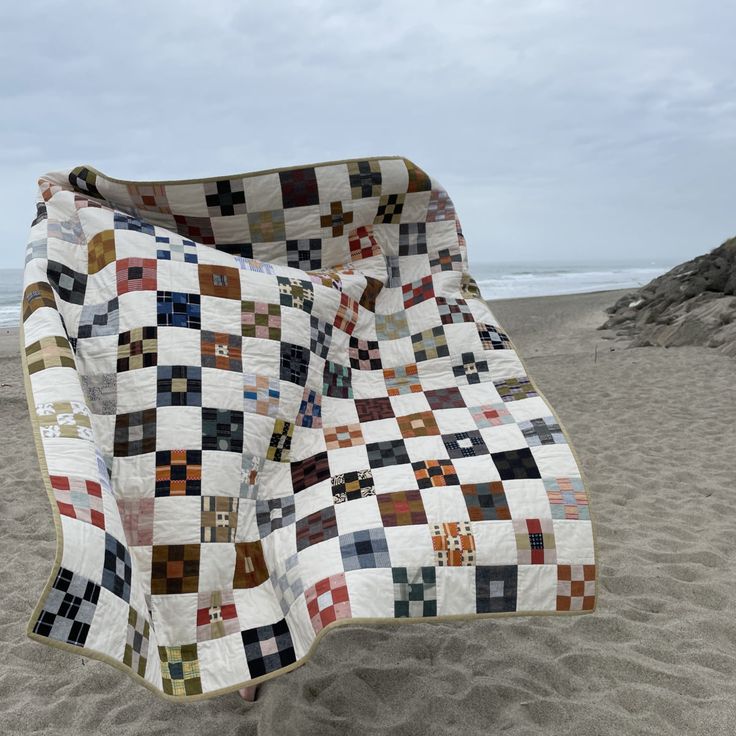 a quilted blanket on the beach with sand in the foreground and water in the background