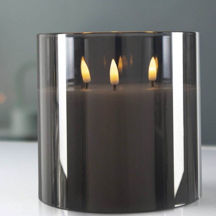 three lit candles in a metal container on a white countertop, with the reflection of another candle behind it