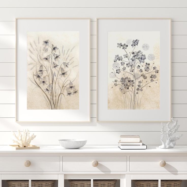 two framed pictures on the wall above a white table with wicker baskets and vases