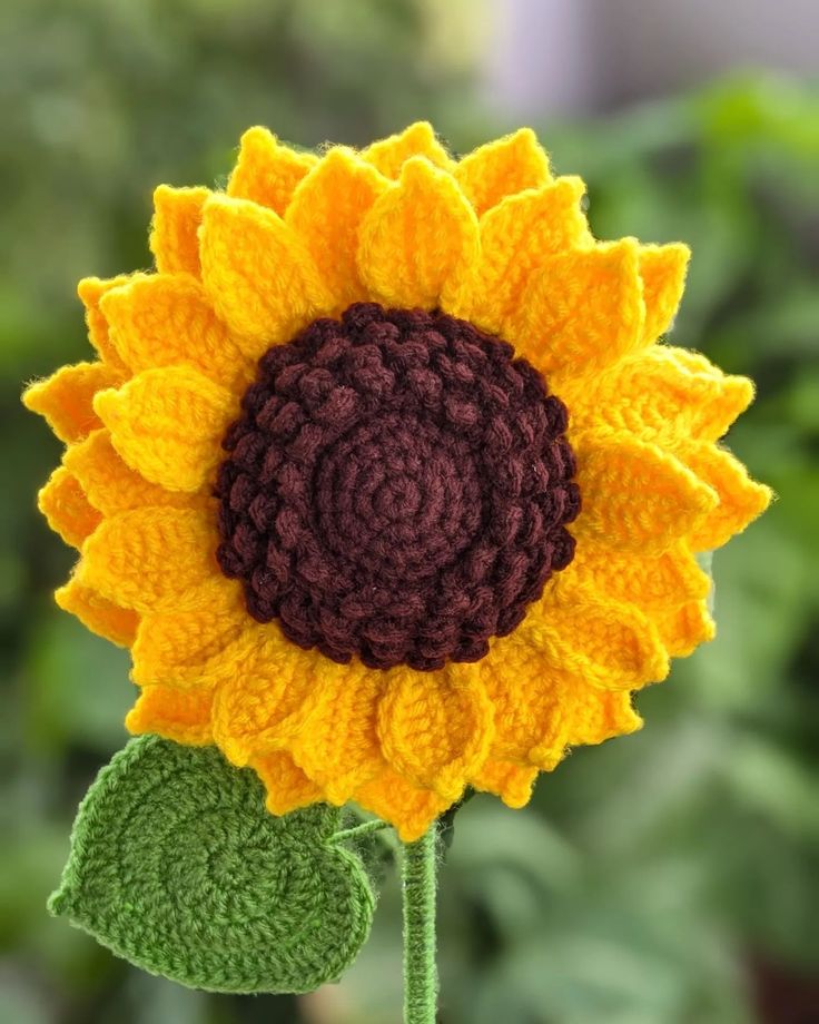 a crocheted sunflower sitting on top of a green plant