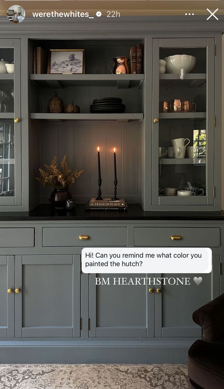 a gray china cabinet with candles and pictures on the wall above it that says, hit can you remind me what color you painted the hutch?