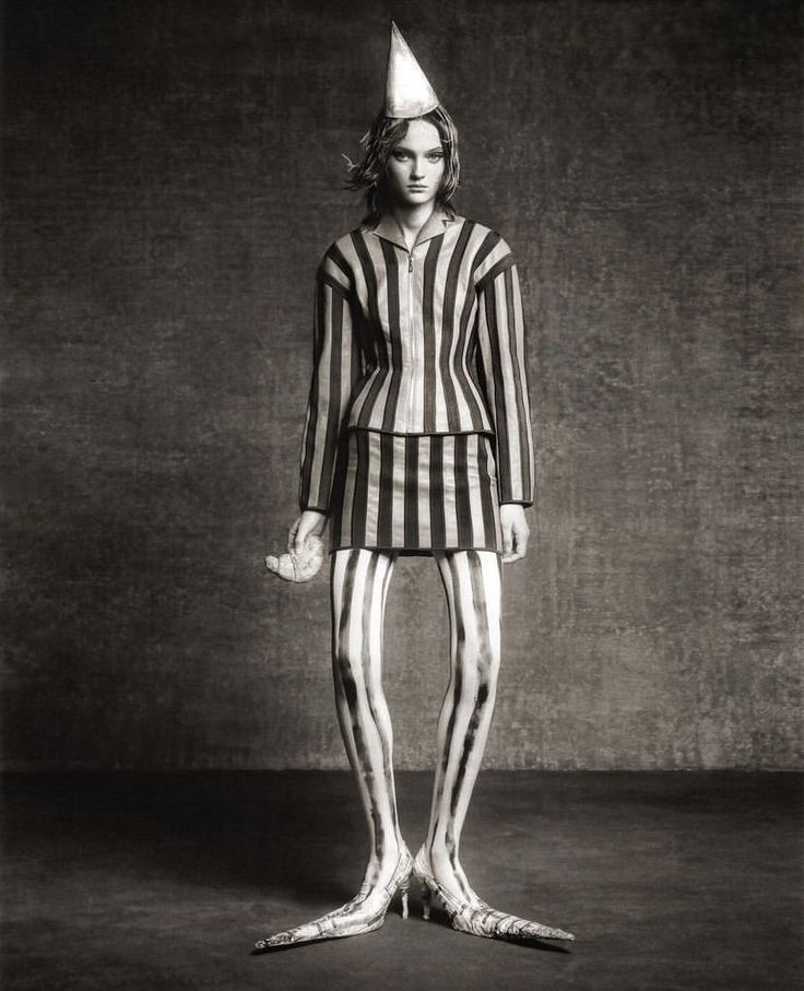 a man in striped clothing with a party hat on his head and legs, standing against a wall