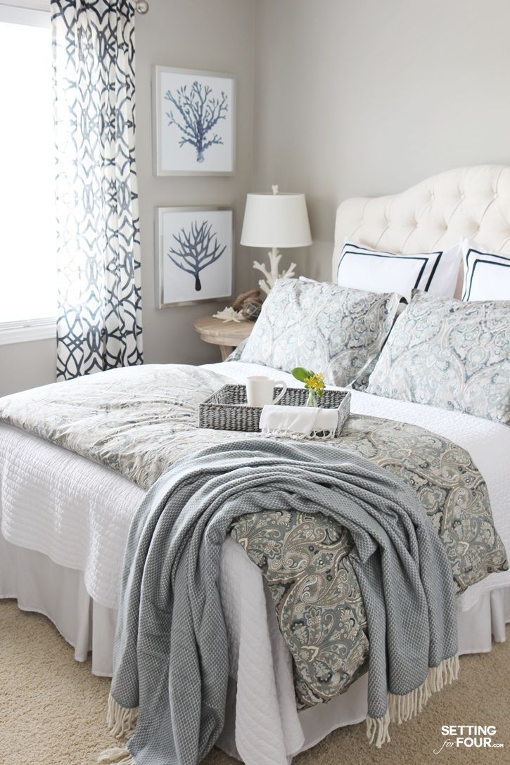 a white bed sitting in a bedroom next to a window with blue and white curtains