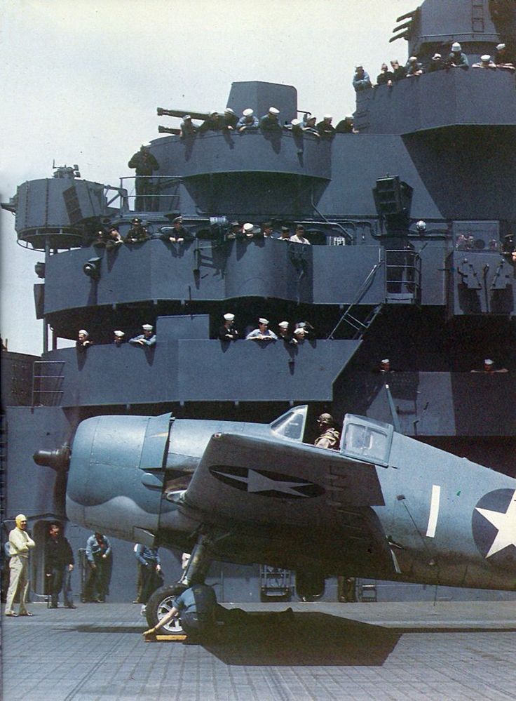 an old navy plane sitting on top of a tarmac next to a large ship