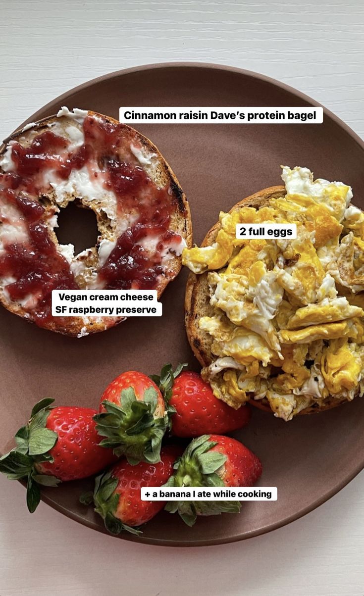 an english muffin with bacon, eggs and strawberries on a brown plate next to some other breakfast foods