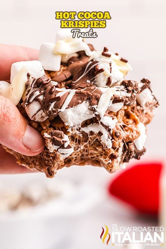 a person holding up a chocolate krispy kreme cookie with marshmallows