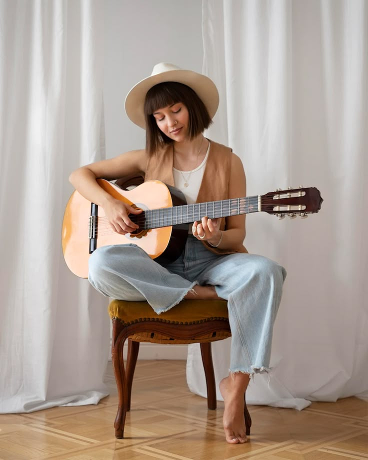 a woman sitting on a chair with a guitar in her lap and wearing a cowboy hat