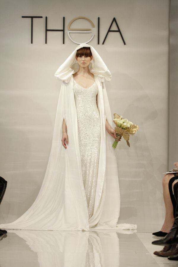 a woman in a white dress and veil walking down the runway with flowers on her head