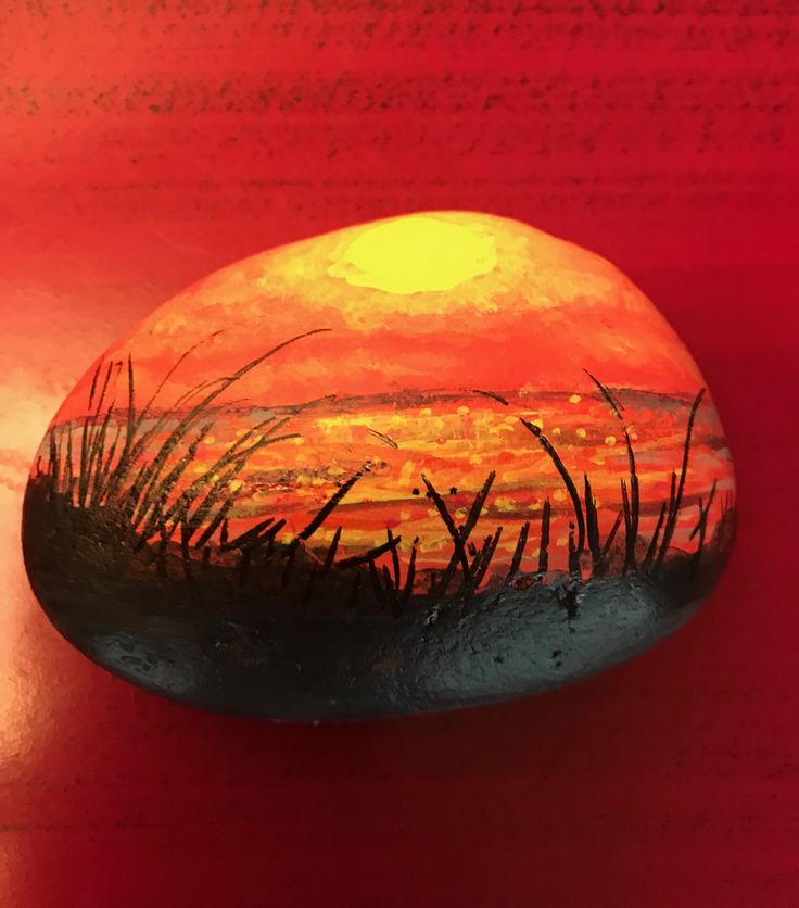 a painted rock sitting on top of a wooden table next to a red wall and grass