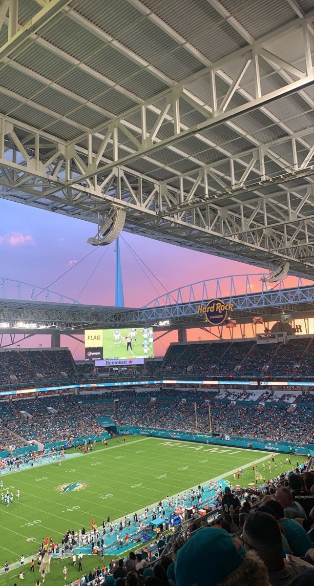 a stadium filled with lots of people watching a football game at sunset or sunrise time