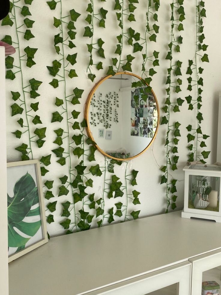 a white desk topped with a mirror next to a wall covered in green ivy leaves