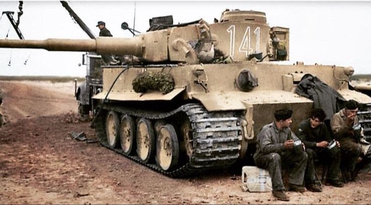 two men sitting next to a tank in the desert