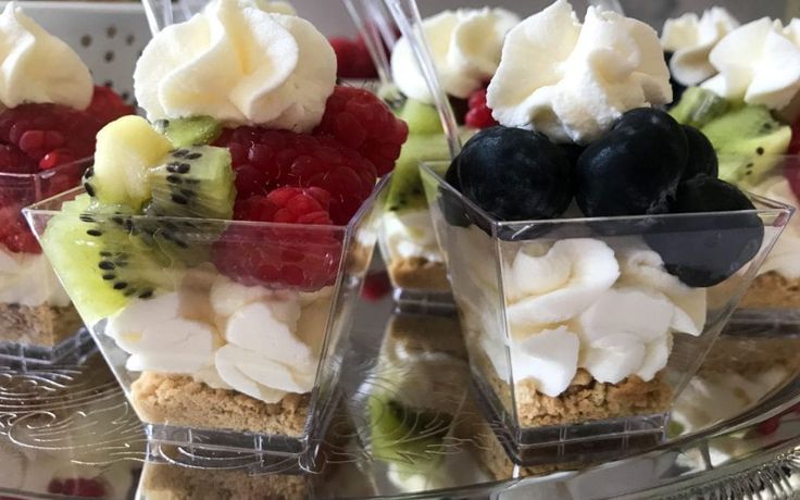 desserts are arranged in small clear containers on a silver platter with fruit and whipped cream