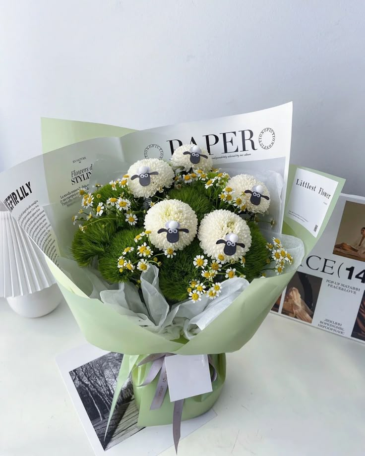 a bouquet of daisies and carnations is wrapped in green paper next to magazines