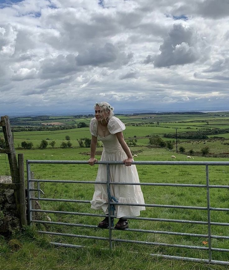 a woman in a white dress leaning on a fence looking over the top of it