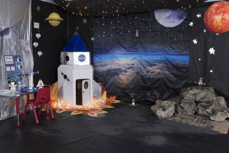 a space themed room with a rocket ship and other items on the floor in front of it