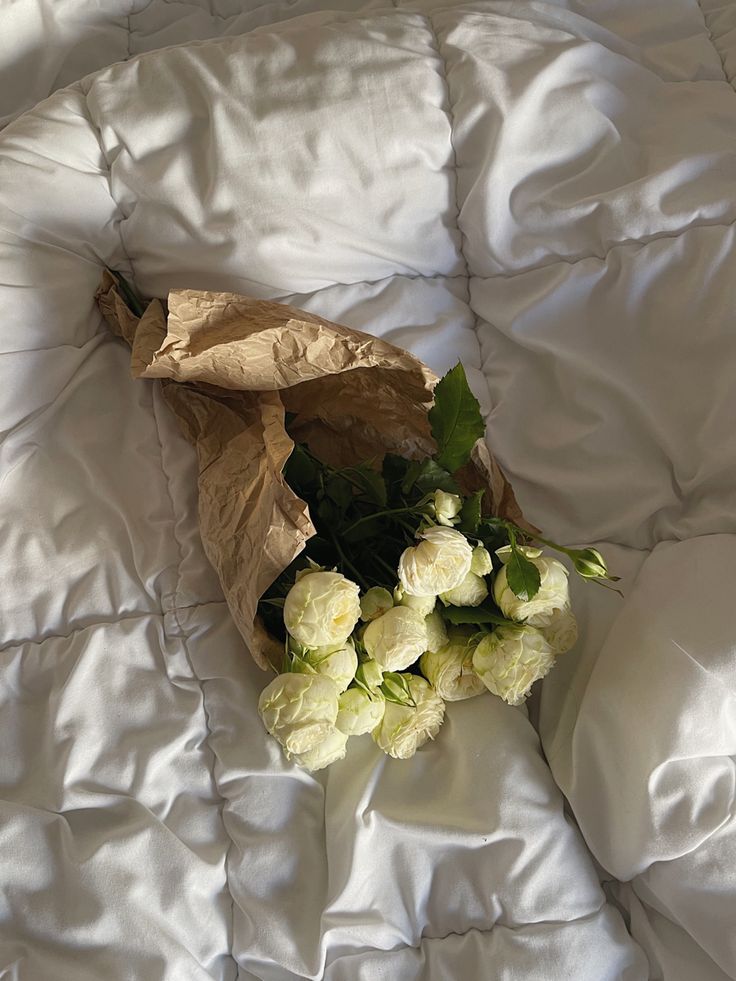 a bouquet of white flowers laying on top of a bed covered in white linens