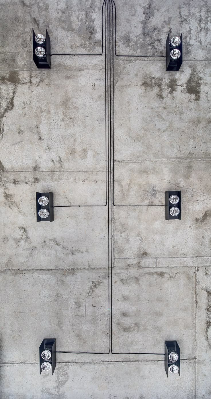 three black and white street lights mounted to concrete wall with wires running through them on either side