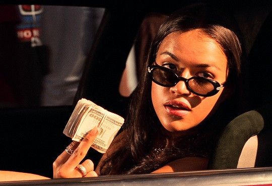 a woman sitting in the back seat of a car holding money and wearing black sunglasses