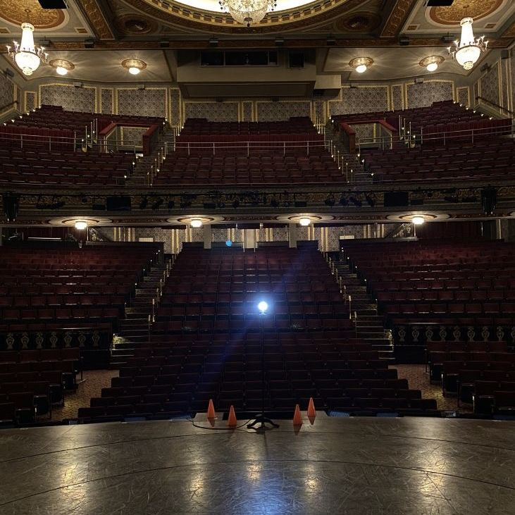 an empty auditorium with lights on the ceiling and no people in seats at the stage