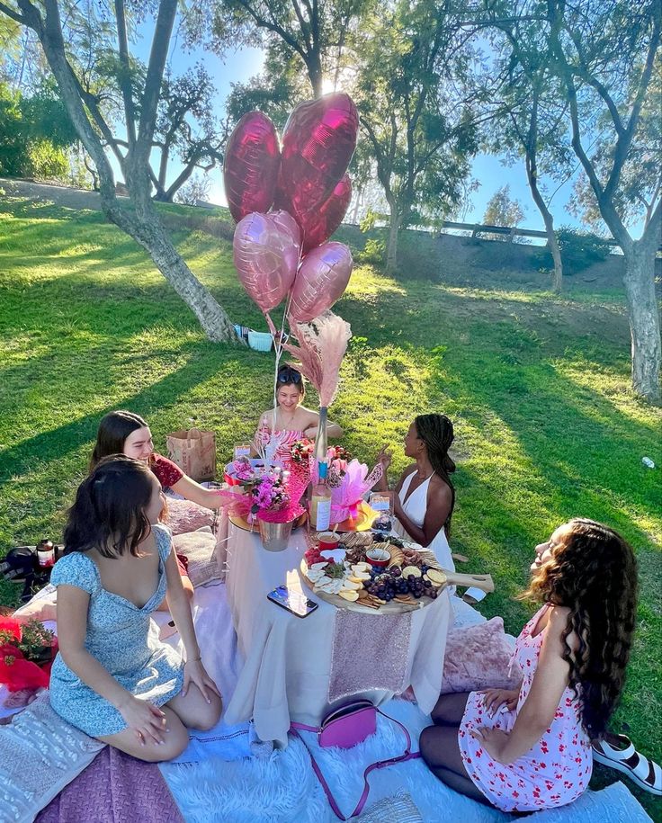 a group of women sitting around a table with pink heart shaped balloons on top of it