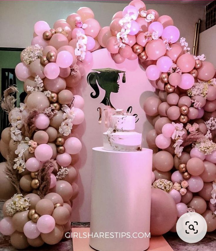 there is a cake on top of a stand in front of some balloons and flowers