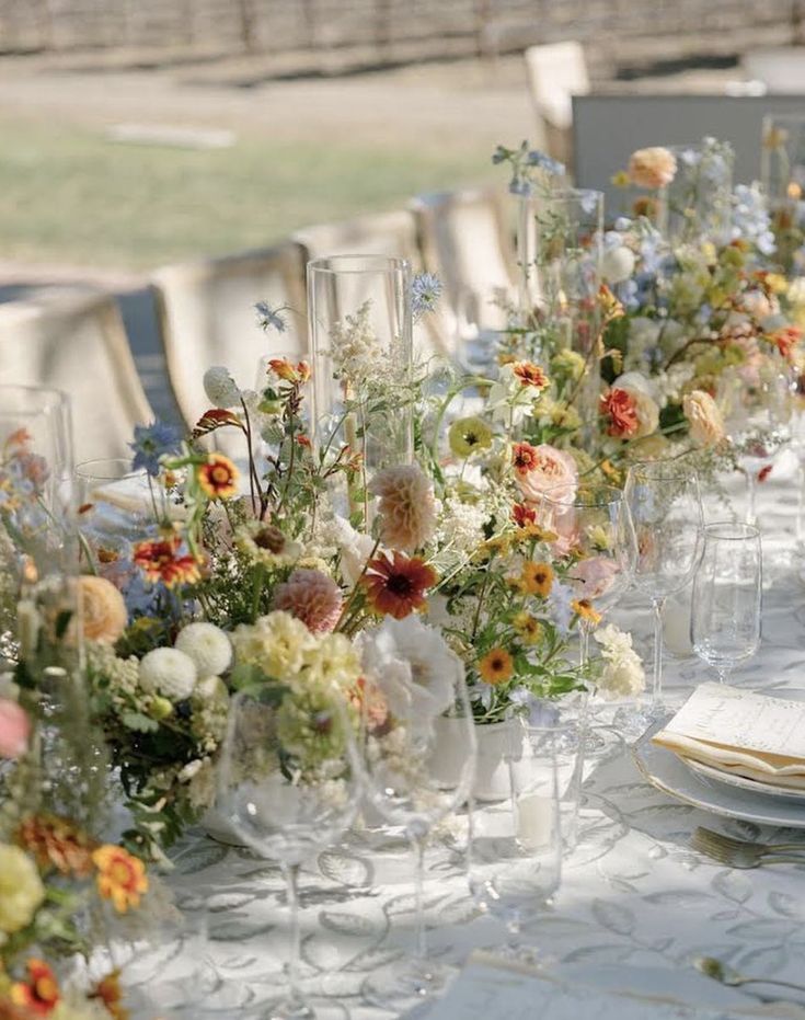 a long table is set with flowers and wine glasses for an elegant wedding reception at the park