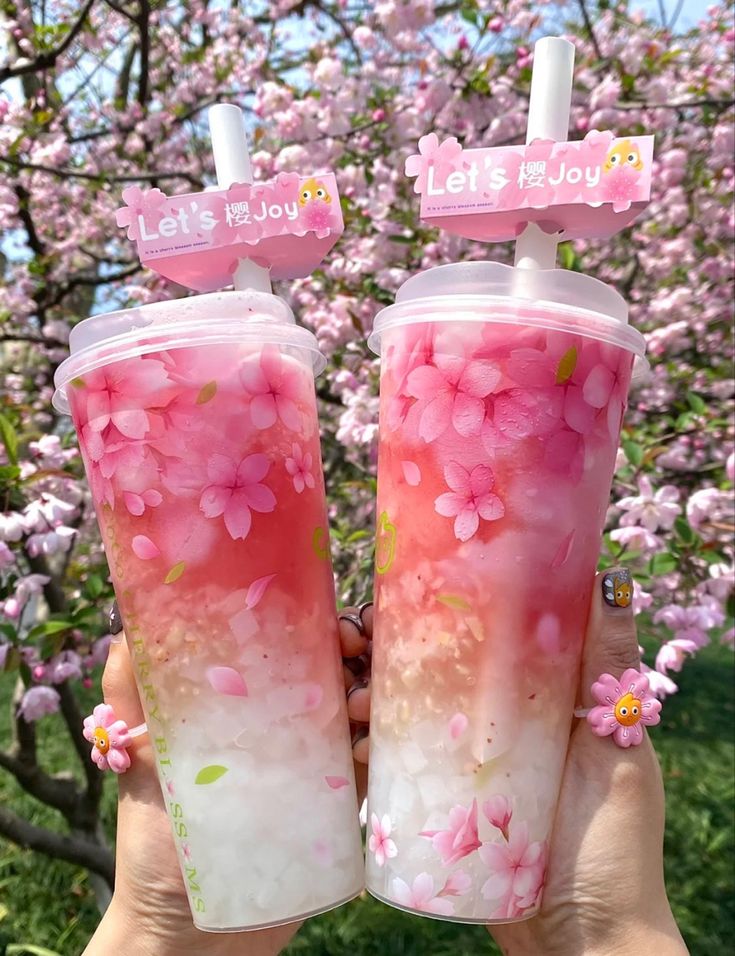 two people holding up cups with pink flowers on them and let's be joy signs