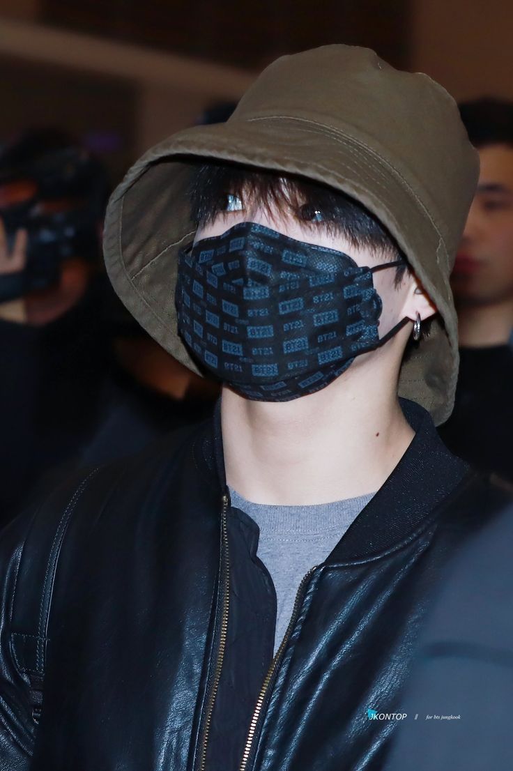 a young man wearing a black face mask with blue letters printed on it, while standing in front of a group of people